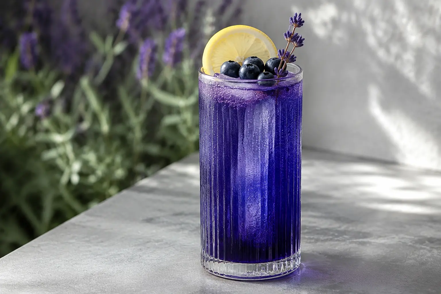 Deep indigo blueberry-lavender tonic mocktail in a ribbed highball glass with clear ice, a lemon wheel, blueberries and culinary lavender